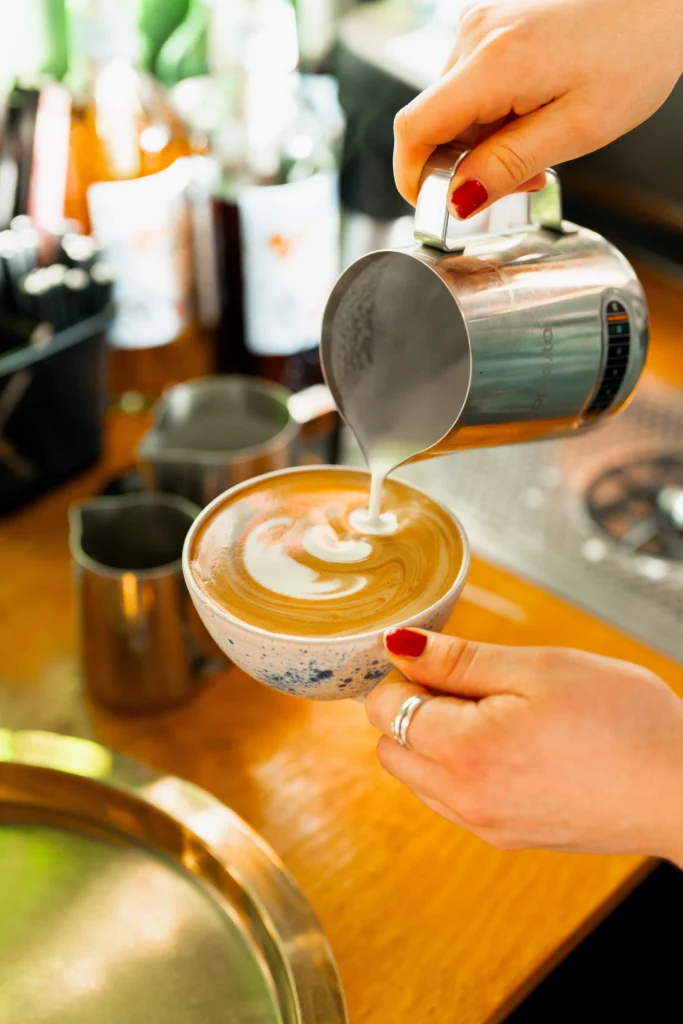 Person laver latteart med mælkeskum, caféstemning